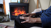 an elderly man warms himself in front of a gas fire
