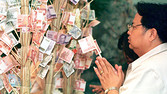 A man, holding a Thai baht bank note, prays before attaching his offering to a "merit tree" at the Bank of Thailand in Bangkok in 1998