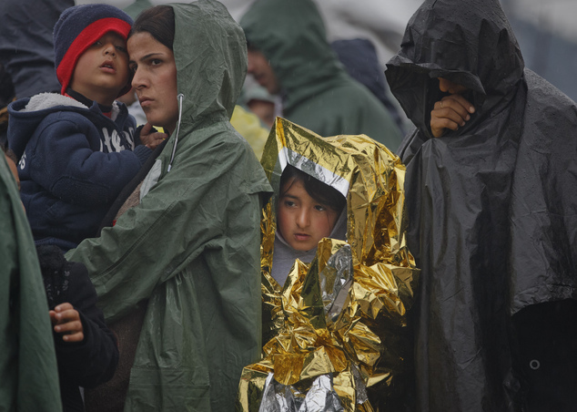 A child wears a thermal blanket while waiting with other migrants in the rain for daily food rations at the northern Greek border station of Idomeni, Sunday,...