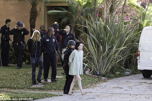 Scantlin is dragged from the property by officers behind a woman wearing a long, white t-shirt 