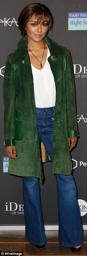 Keeping warm: Kat Graham had flung a long green coat over her own V-neck, top, which was white and tucked into high-waisted jeans with flared hems