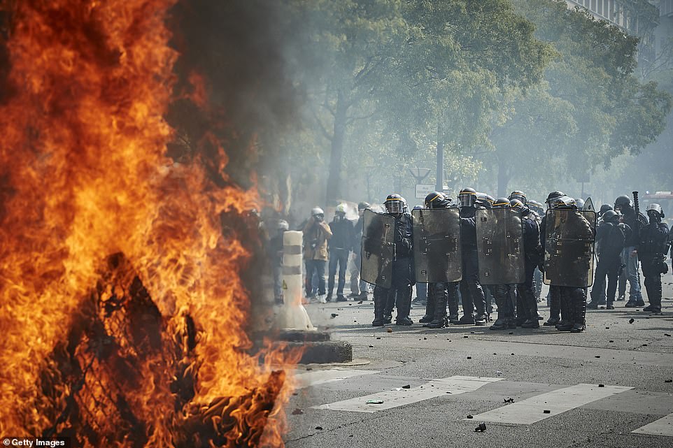 French Riot Police stand in clouds of tear gas near a burning barricade as demonstrators set fire to rubbing bins and vehciles around Paris