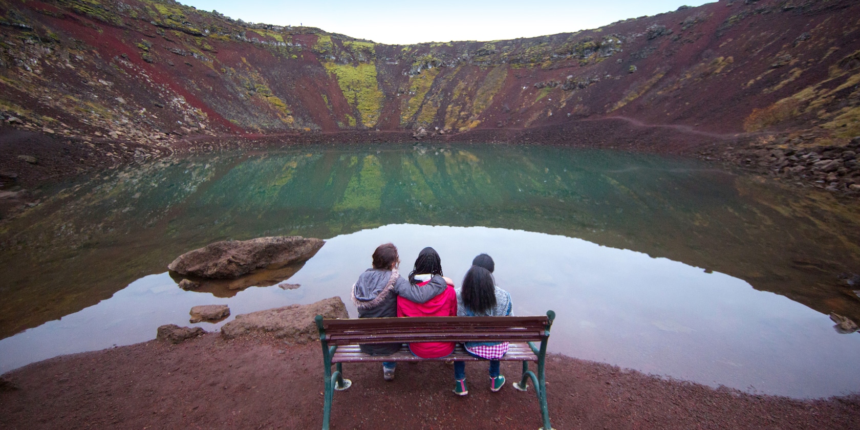 Three girls sitting on a bench overlooking a volcanic crater lake in Iceland