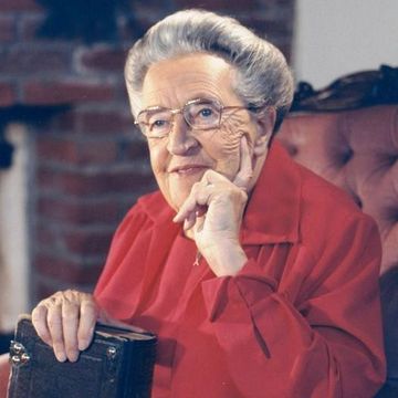 corrie ten boom sitting in a chair while resting her head in her left hand and holding a book