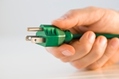 A human hand holds a green electrical plug.