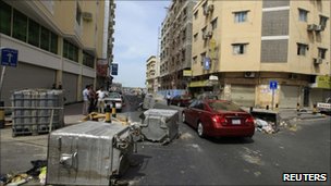 Cars pass garbage containers thrown onto the road in Manama 15 March