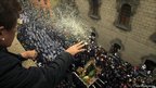 A woman throws petals from a building onto a procession through a street below