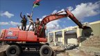 Mechanical digger breaks wall of Bab al-Aziziya compound