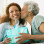 Mother kissing adult daughter, holding present C. Barry Austin Photography