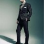 De perfil y erguido, Chris Evans luce un traje color plomo con corbata gris y camisa de estampado a cuadros con zapatos de cintas color negro.