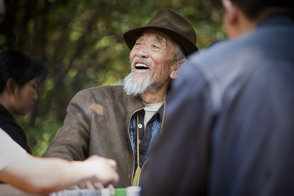 A man smiles at a park table in Kunming playing Mahjong