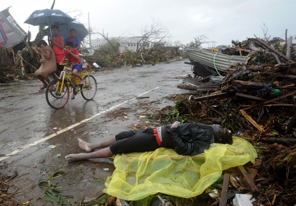 Children ride by a dead body on a street in Tacloban, Philippines. 