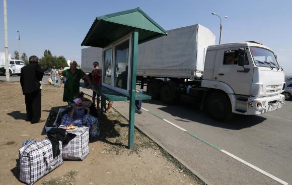 Trucks of a Russian convoy carrying humanitarian aid for Ukraine drive onto the territory of Russia-Ukraine border crossing point 'Donetsk', with people who have fled from fighting in eastern regions of Ukraine seen nearby, in Russia's Rostov Region, August 22, 2014. REUTERS/Alexander Demianchuk