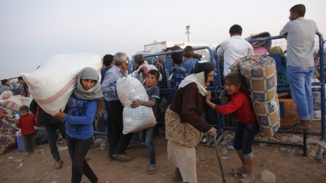 Newly arrived Syrian Kurdish refugees carry their belongings after crossing into Turkey