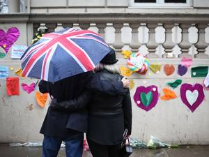 8 January 2015: A man who had just placed a pair of pencils and a note offering sympathy to the victims of the Paris shootings on a wall at the French Embassy stands with a woman in contemplation under a Union flag umbrella in London
