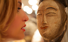 A woman stares into the tribal art sculpture of a face at the 2014 London Tribal Art exhiition at Mall Galleries
