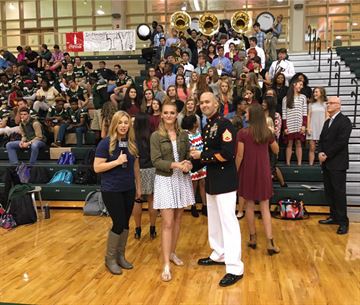 Staff Sgt. Clifford M. Lucker presents Carol Turner with the March to Greatness challenge coine during the live airing of the pep rally Oct. 21, 2016, at River Bluff High School in Lexington, South Carolina.   Turner, a snare drum player and band president, earned the recognition for the hard work and dedication she shows during marching band and in her community. Lucker is a canvassing recruiter at Marine Corps Recruiting Station Columbia. (Official Marine Corps photo by Sgt. Tabitha Bartley/Released)
