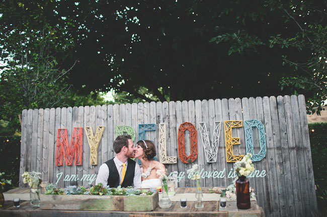 Bride and groom in front of DIY 'My Beloved' sign on reclaimed wood