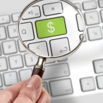 Keyboard with dollar sign key shown through magnifying glass. (iStock)
