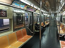 The interior of an R62 car on the 3 train. Its seats are yellow and orange, with several advertisements hanging above.