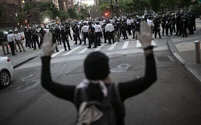 A protester raises her hands as police start to arrest demonstrators refusing to get off the streets during an imposed curfew while marching in a solidarity rally calling for justice over the death of George Floyd, on June 2, 2020, in New York. (AP Photo/Wong Maye-E via Jewish News/via The Times of Israel)