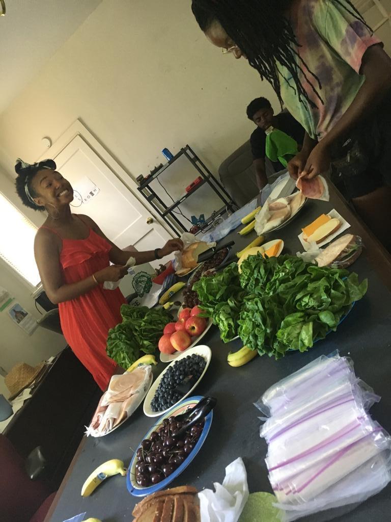 Black woman smiling while placing food on long table with beautiful fresh herbs and produce.