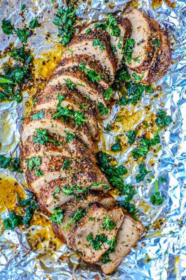 picture of a sliced pork tenderloin with parsley on top of aluminum foil 