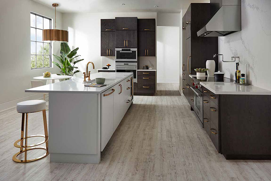Modern themed kitchen with dark stained cabinets, stainless steel appliances, and grey colored island on luxury vinyl plank flooring.