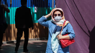 An Iranian woman wearing a protective mask adjusts her head scarf as she walks on a street in Tehran on April 12, 2021