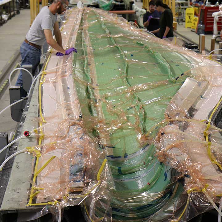 A cross-section of a long wind blade covered in plastic. Three researchers work in the distance.