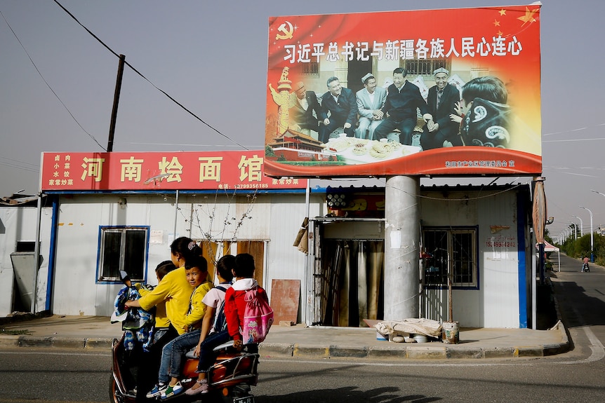 A woman rides a motorbike with several children as they ride past a picture showing China's President Xi Jinping
