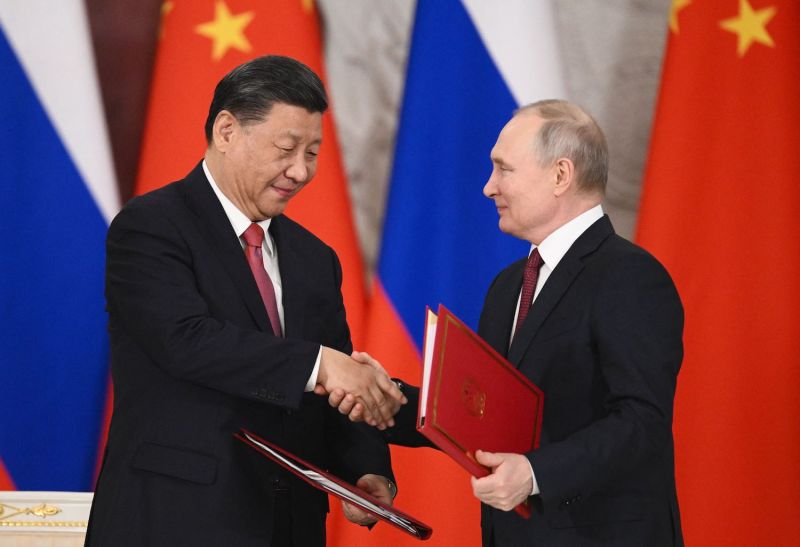 Xi and Putin shake hands while carrying red folders.